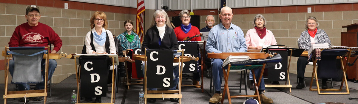 Corydon Dulcimer Society members setting in a group preparing to play while smiling towards the camera